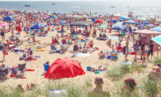 A busy beach full of people with tents, towels and parasols on the sand and swimming.