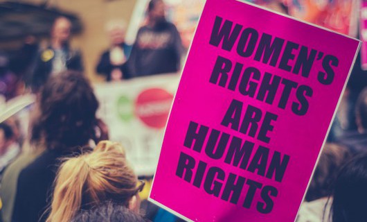 A large pink poster which says 'Women's rights are human rights' is shown at a march.