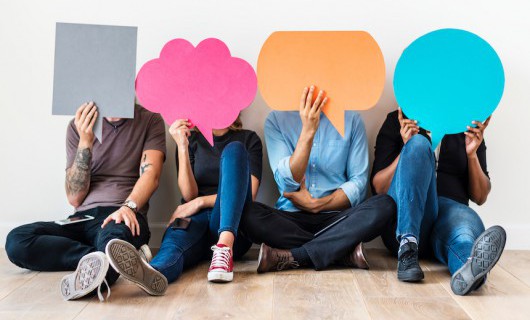 Four people are sat holding different shaped speech bubbles in front of their faces.