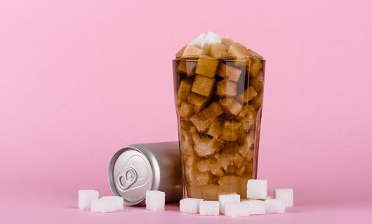 A can on its side is beside a glass overfilled with coke and sugar cubes.