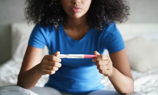A young girl sits on her bed, staring at the pregnancy test in her hands.