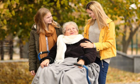 A smiling girl, woman and older lady in a mobility scooter take a stroll in a park.