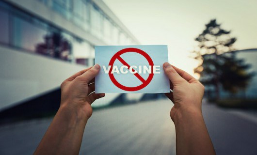 Two hands hold a piece of paper showing a 'banned' red circle symbol striking out the word vaccine.