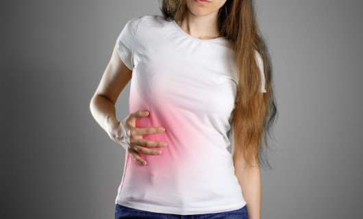 A woman in a white shirt is clutching the right side of her stomach, which glows red.