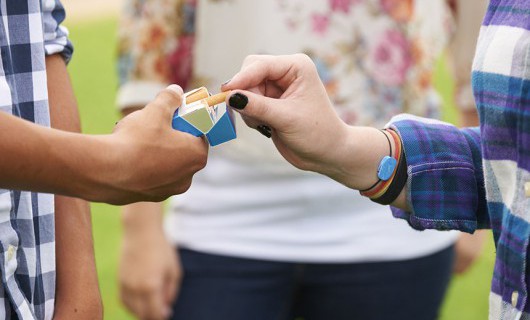 The hand of a young adult is holding a packet of cigarettes as someone takes one from the packet.