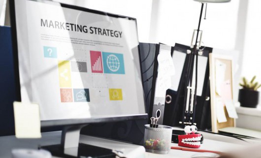 A computer screen on an office desk displays the words 'marketing strategy'.