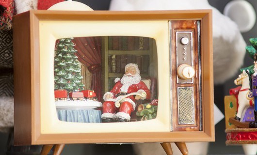 A Christmas ornament of a television showing Santa Clause sat beside a decorated tree.