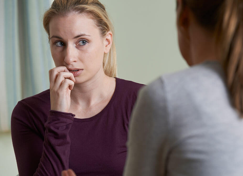 A woman looks concerned and holds her face as she speaks to her therapist.