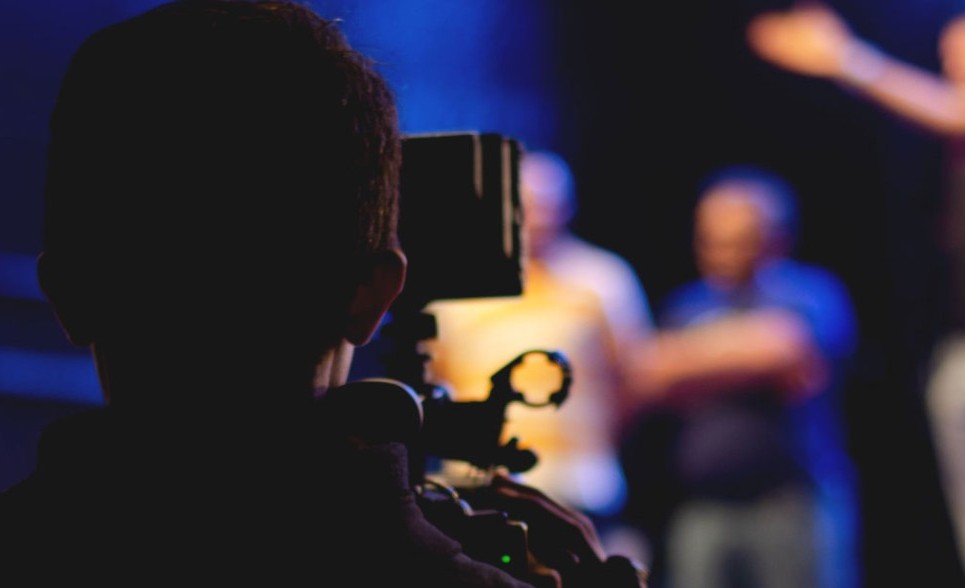 A view from behind a videographer filming performers on a stage.