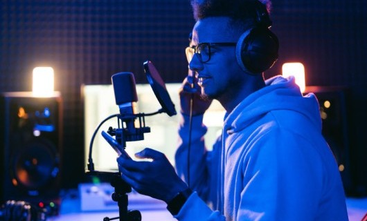 A young singer in a recording studio, reading lyrics off their phone.