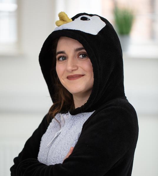 Social Change UK's Researcher, Daisy, poses in a penguin onesie, smiling forwards.