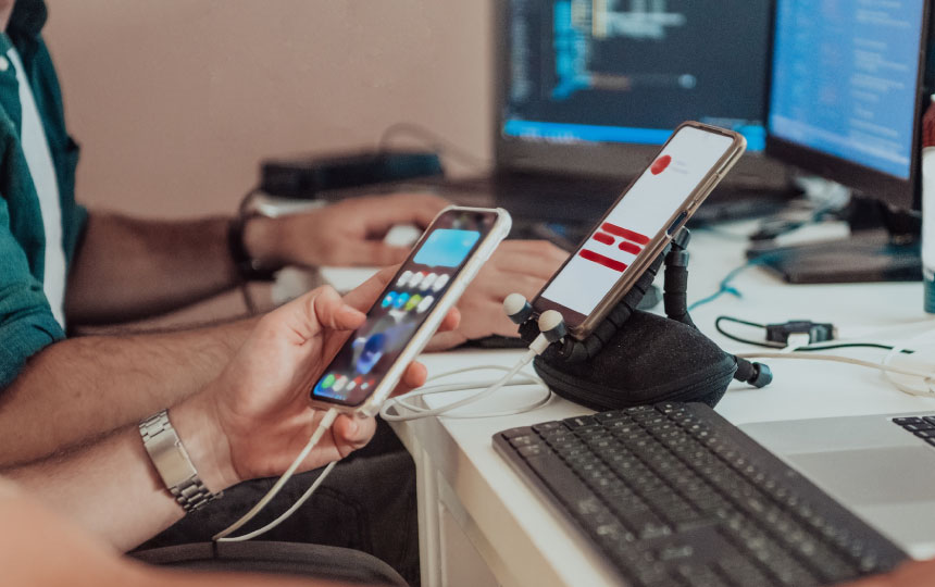 Two people sit at a desk testing a new smart phone app across 2 different phones.