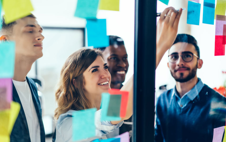 A group of people draw and write ideas on sticky notes on a clear glass wall.